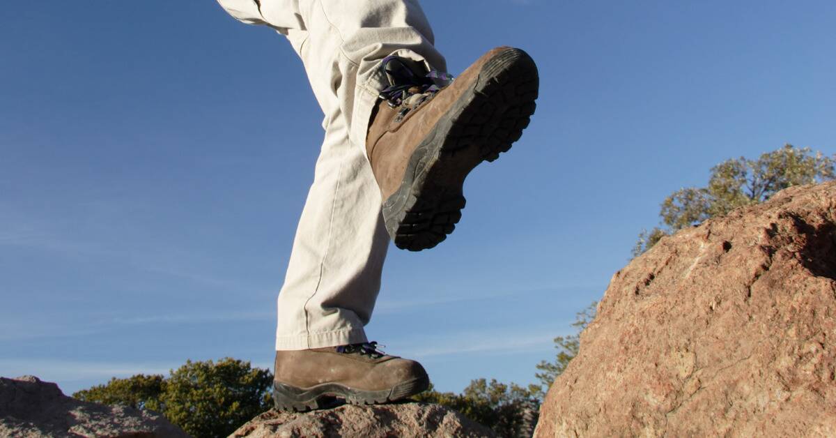 Someone in hiking boots taking a large step atop some rocks.