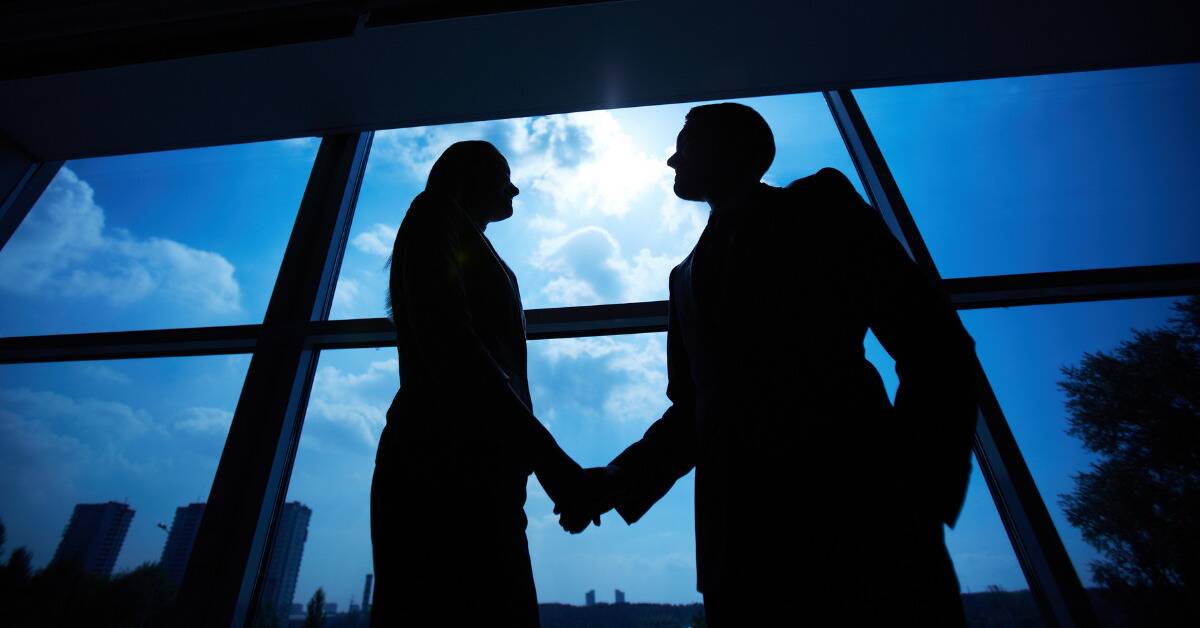 A low angle shot of a silhouette of two business people shaking hands.