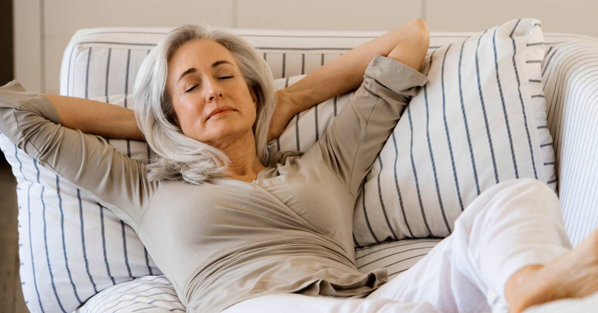 A woman lounging back on her couch, eyes closed, hands behind her head.