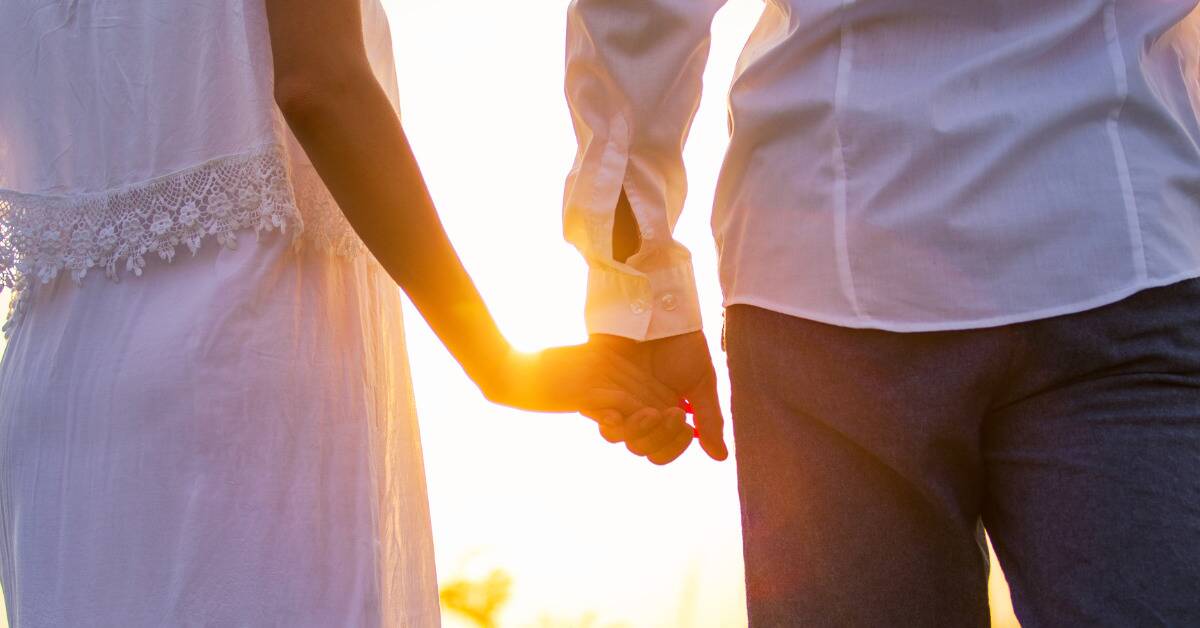 A couple holding hands in front of a sunset.