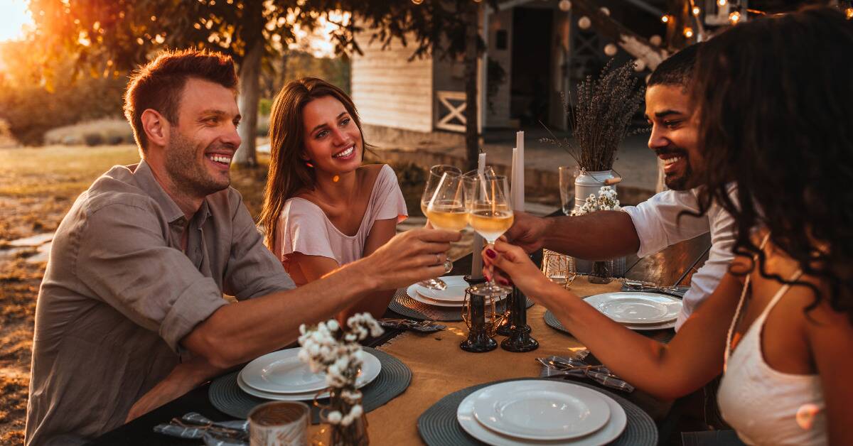 A group of friends all gathered around an outdoor table, cheers-ing their wine glasses together.