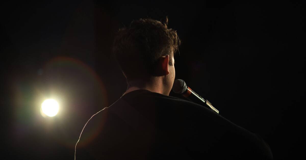 A shot from behind of a person at a microphone, a spotlight shining on them from the side.