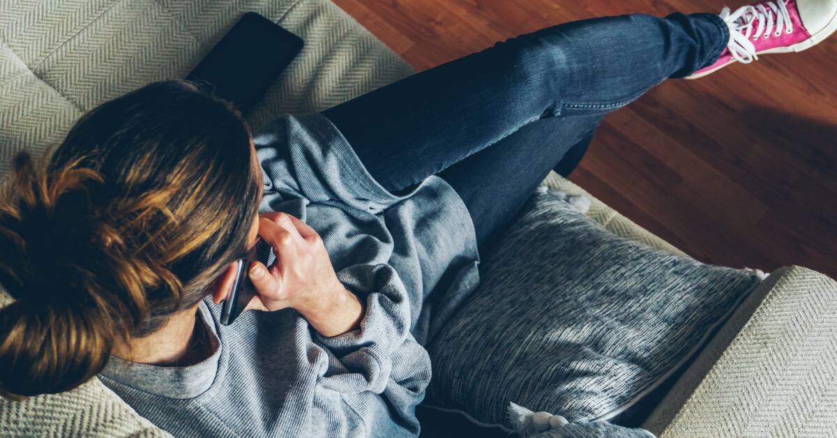 An above shot of a woman talking on her cell phone while sitting on a couch.