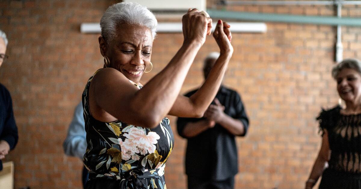 An older woman dancing while friends watch and cheer her on.