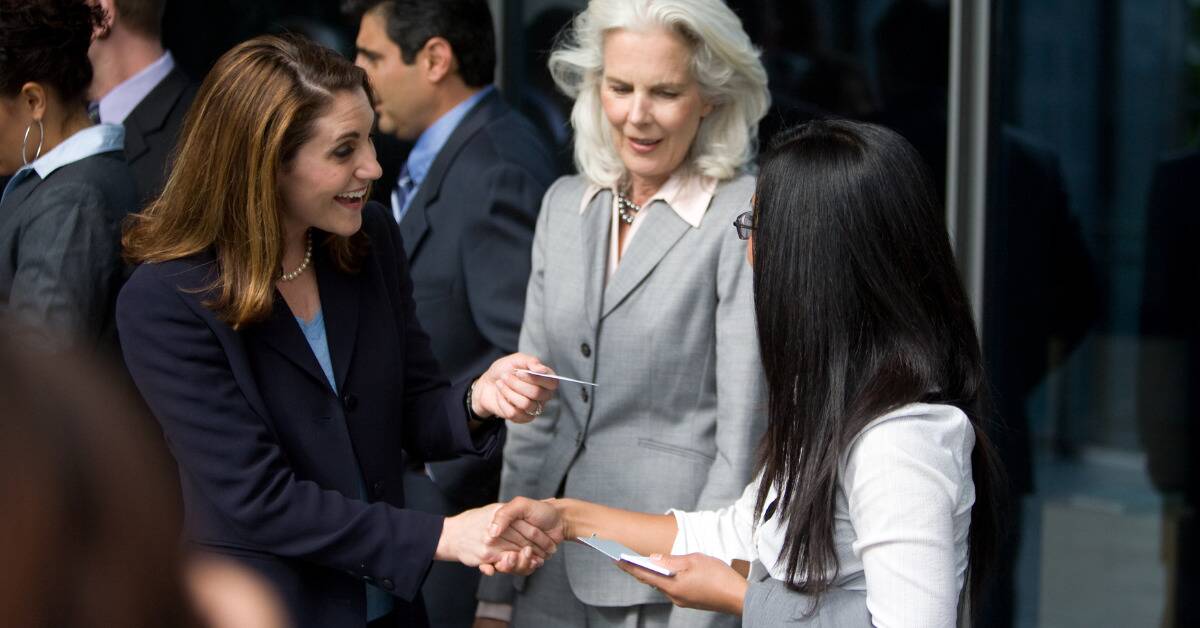 Two women shaking hands and exchanging business cards at a networking event.