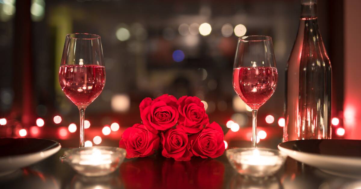 Two glasses of rose on a table, a small bouquet of red roses placed between them.