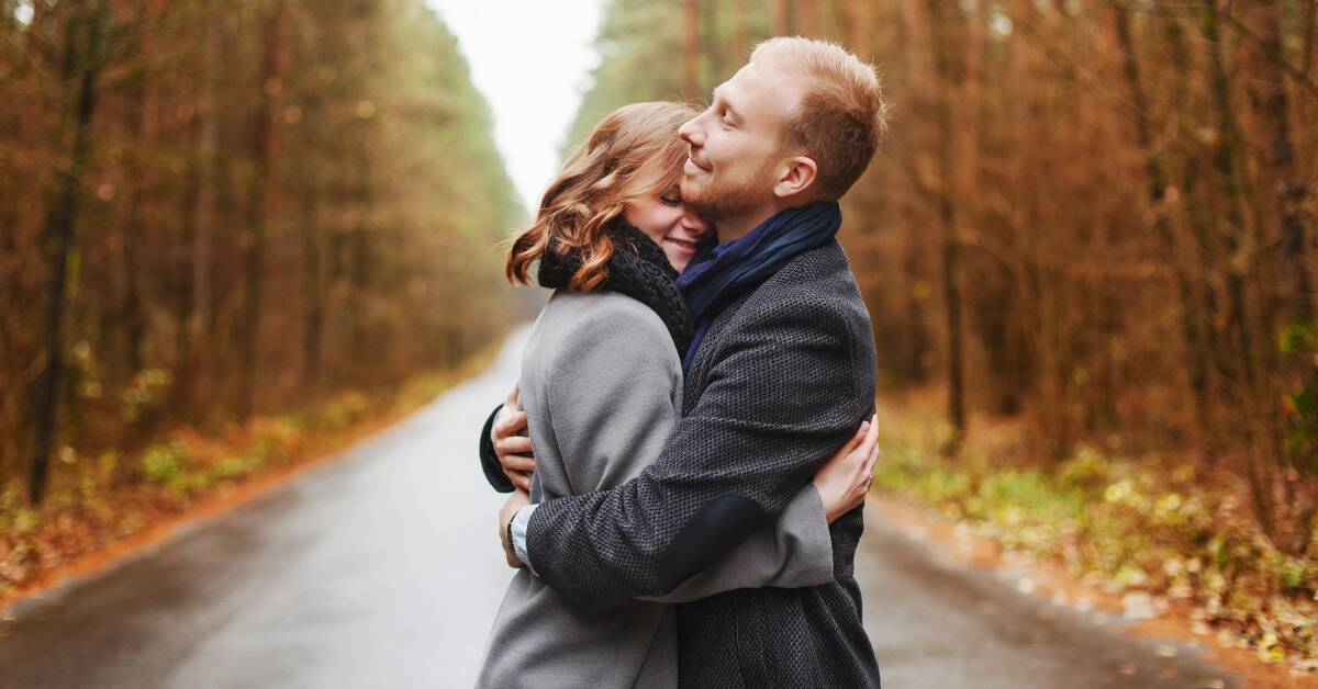 A couple embracing on a tree-lined road.