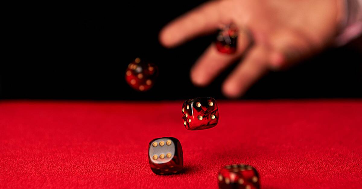 A hand throwing red and black dice on a red table.