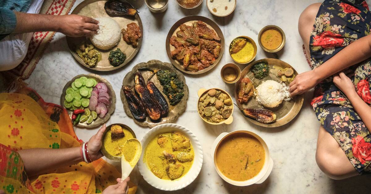 An array of plates full of food on the ground, where people are sitting next to them, reaching out to gather food, shot from above.