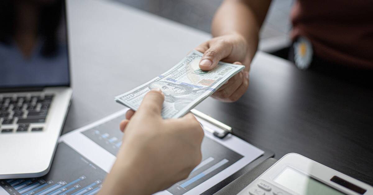 Two people exchanging a stack of $100 bills across a desk.