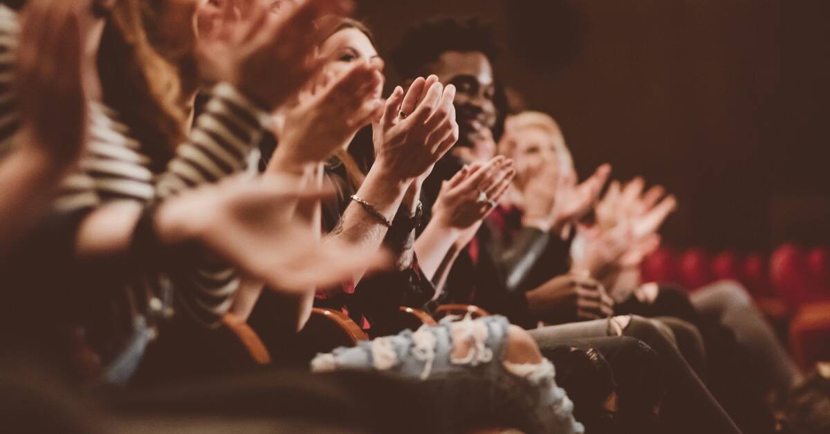 A row of people seated in a theater applauding.