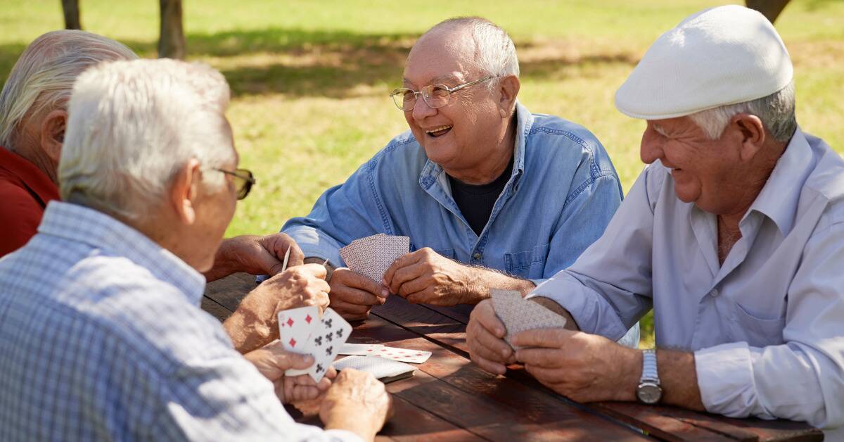 Older men gathered around a park table playing cards.
