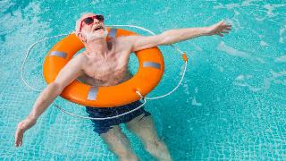 An older man using a life preserver to float in a pool, arms outstretched, looking at the sky.
