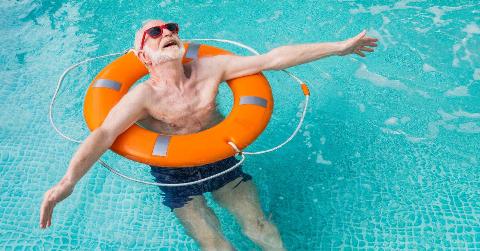 An older man using a life preserver to float in a pool, arms outstretched, looking at the sky.