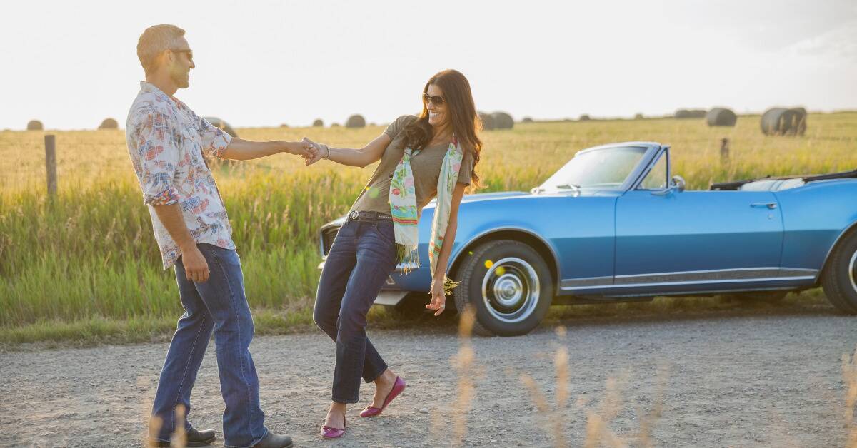 A couple dancing outside in front of a blue, vintage car.