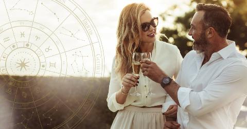 A couple chatting as they cheers two glasses of champagne, free arms linked together, a golden astrology wheel superimposed on the left side of the image.