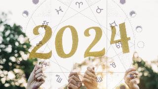 Hands holding up gold numbers that spell out 2024. There's a semi-transparent astrological wheel superimposed on top.