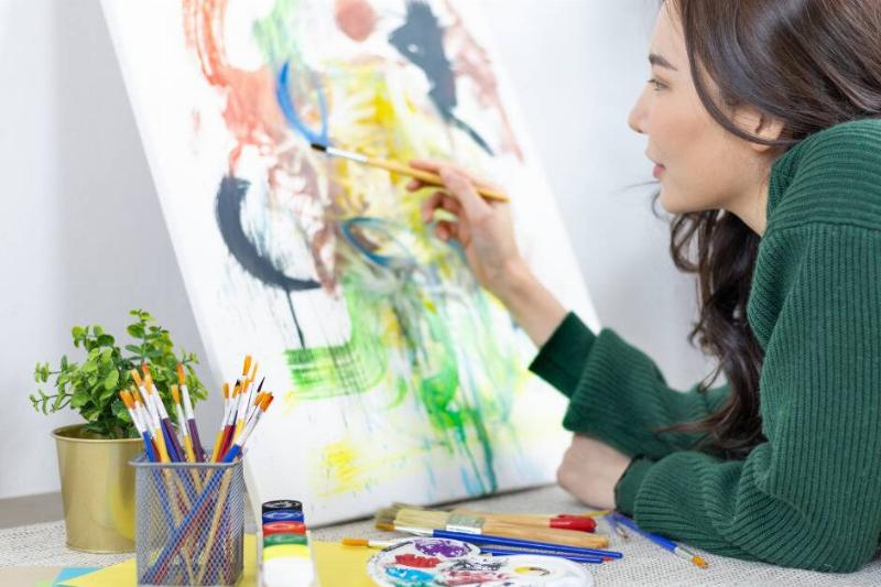 Woman in green sweater using a brush to paint a canvas.
