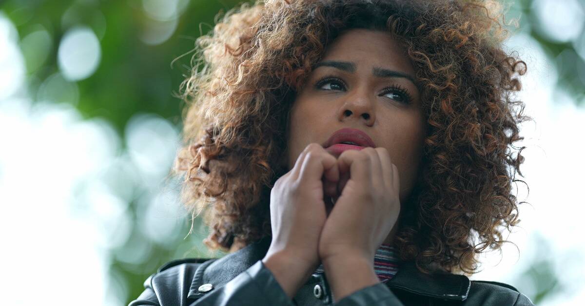 A close, low angle shot of a woman's face. She appears anxious, he hands up by her chin.