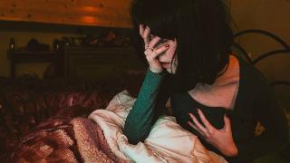 A woman sat up in bed, one hand on her face, one on her chest, as if she'd just woken up in a panic.