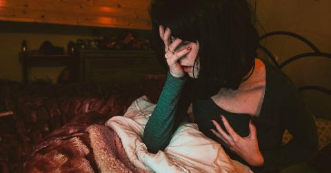 A woman sat up in bed, one hand on her face, one on her chest, as if she'd just woken up in a panic.