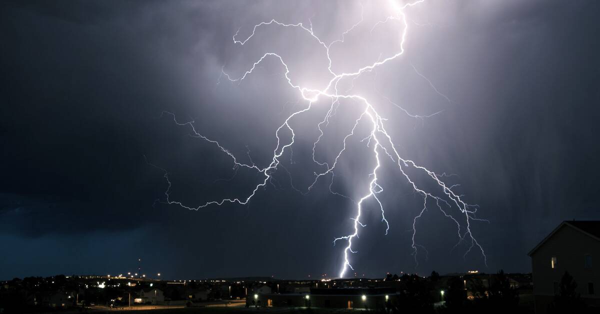 A large lightning strike spreads across the sky above a town.