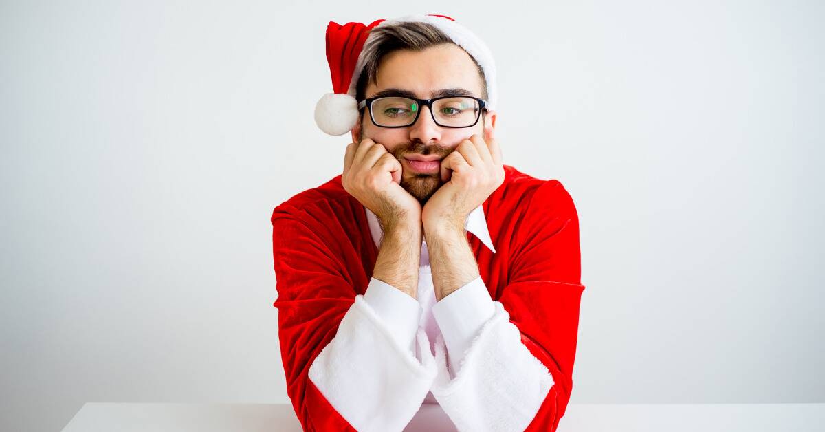 A man in a Santa outfit with his chin in his hands, looking bored.