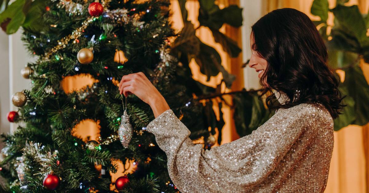 A woman in a sparkly silver shirt decorating a Christmas tree.