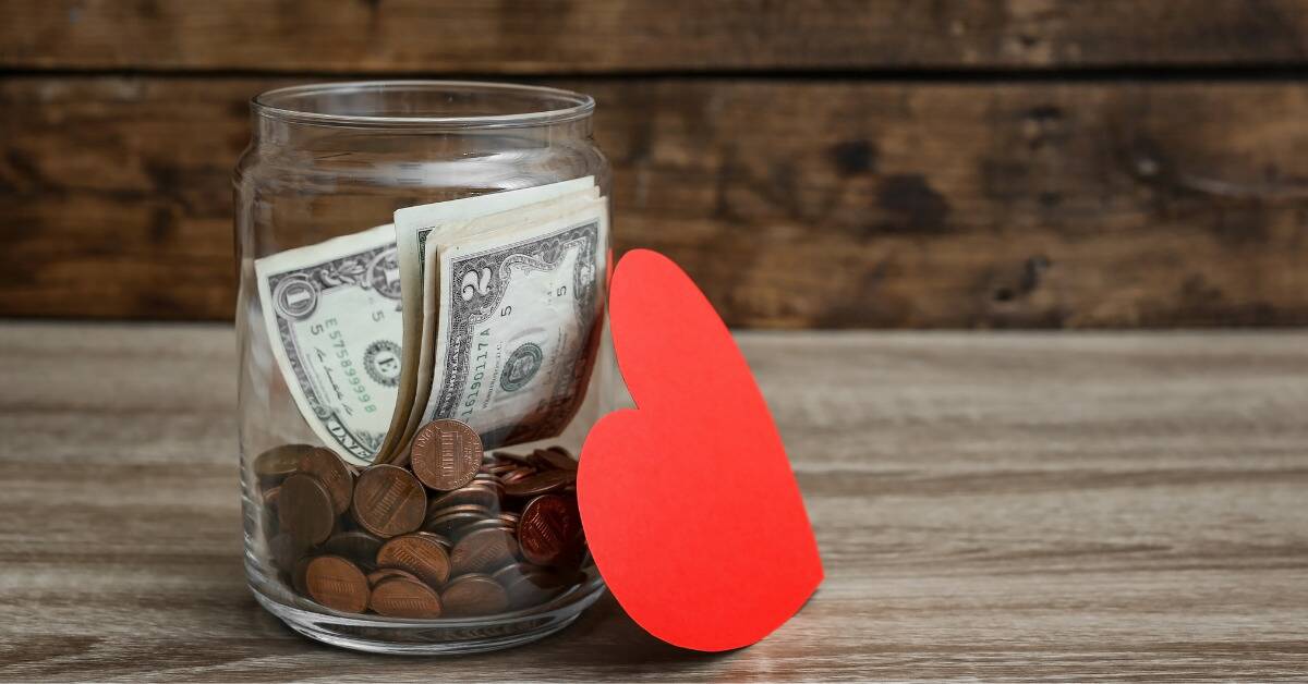 A jar of cash and coins with a red paper heart next to it.