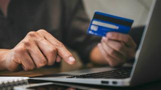 Someone holding their credit card in one hand and typing on their laptop with the other.