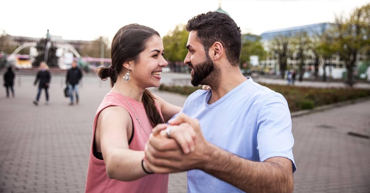 A couple waltzing in public, both smiling.