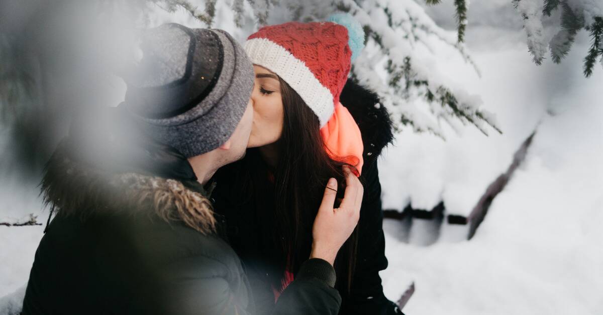 A couple kissing outside in the snow.