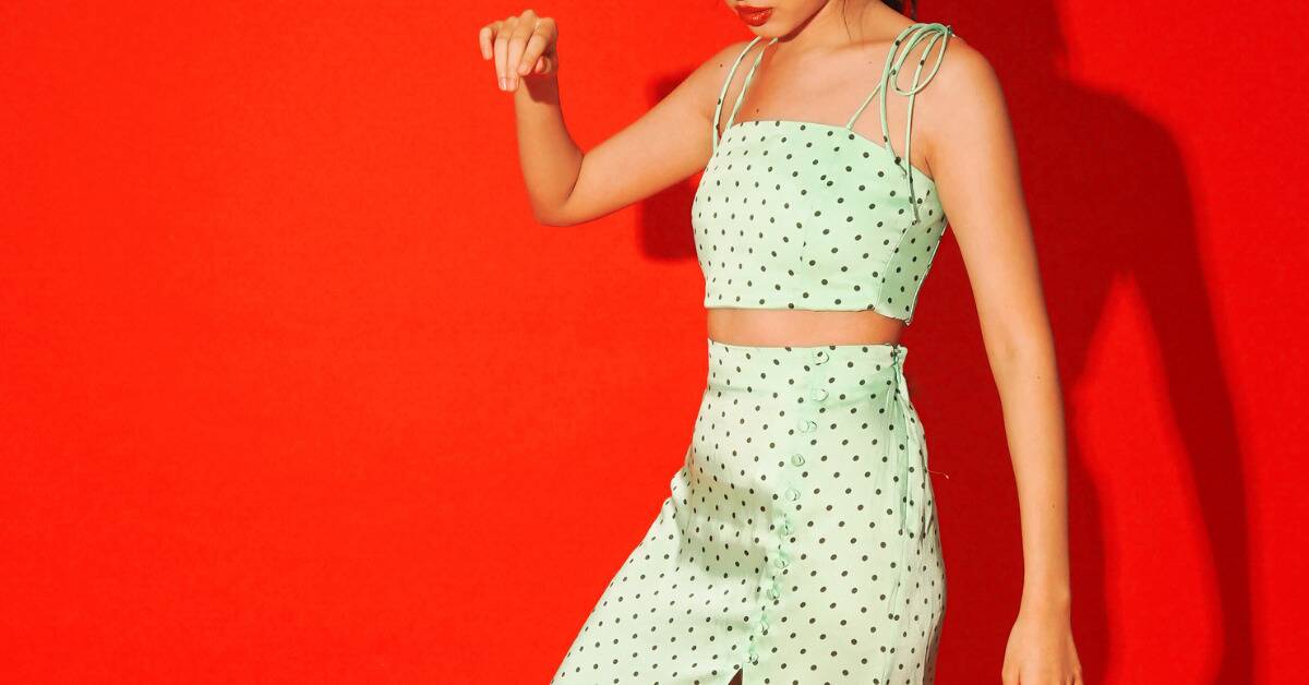 A woman in a light green, polka-dotted two-piece outfit against a bright red background.