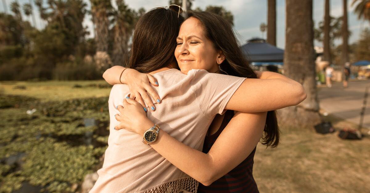 Two women hugging, the one whose face we can see looking loving and emotional.