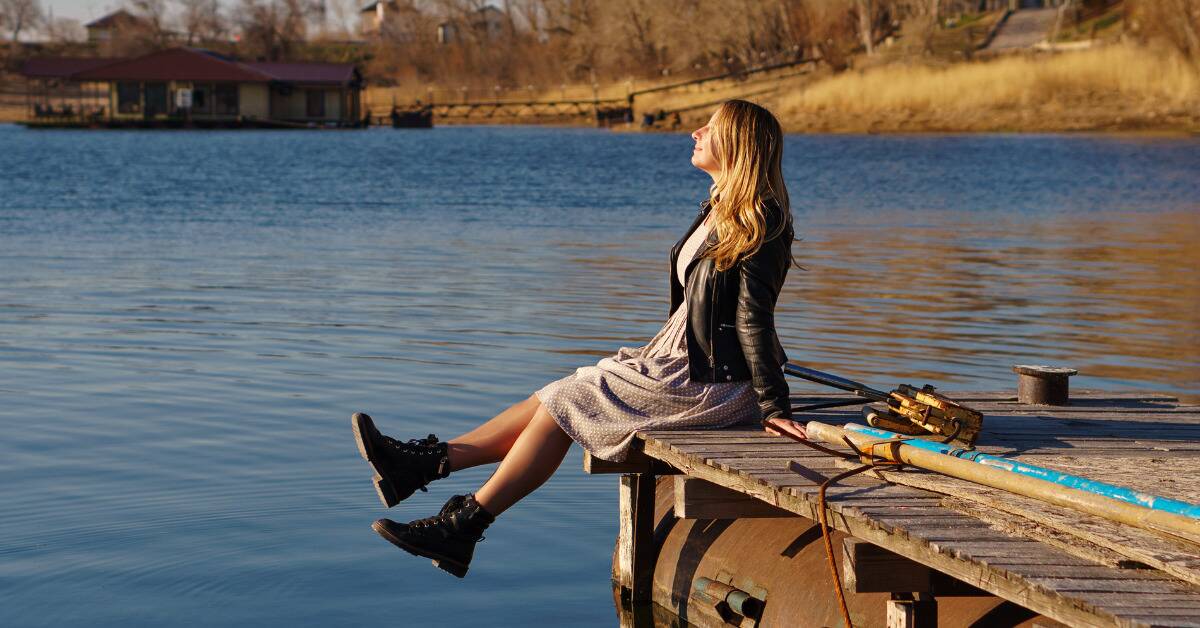 A woman sitting on a dock atop the water, kicking her feet and smiling as she looks upward.