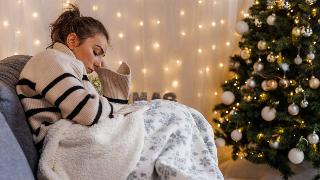 A woman sitting on a couch next to her Christmas tree, looking sad.