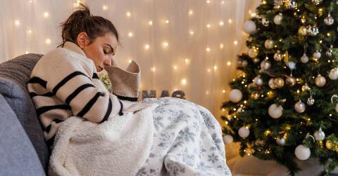 A woman sitting on a couch next to her Christmas tree, looking sad.