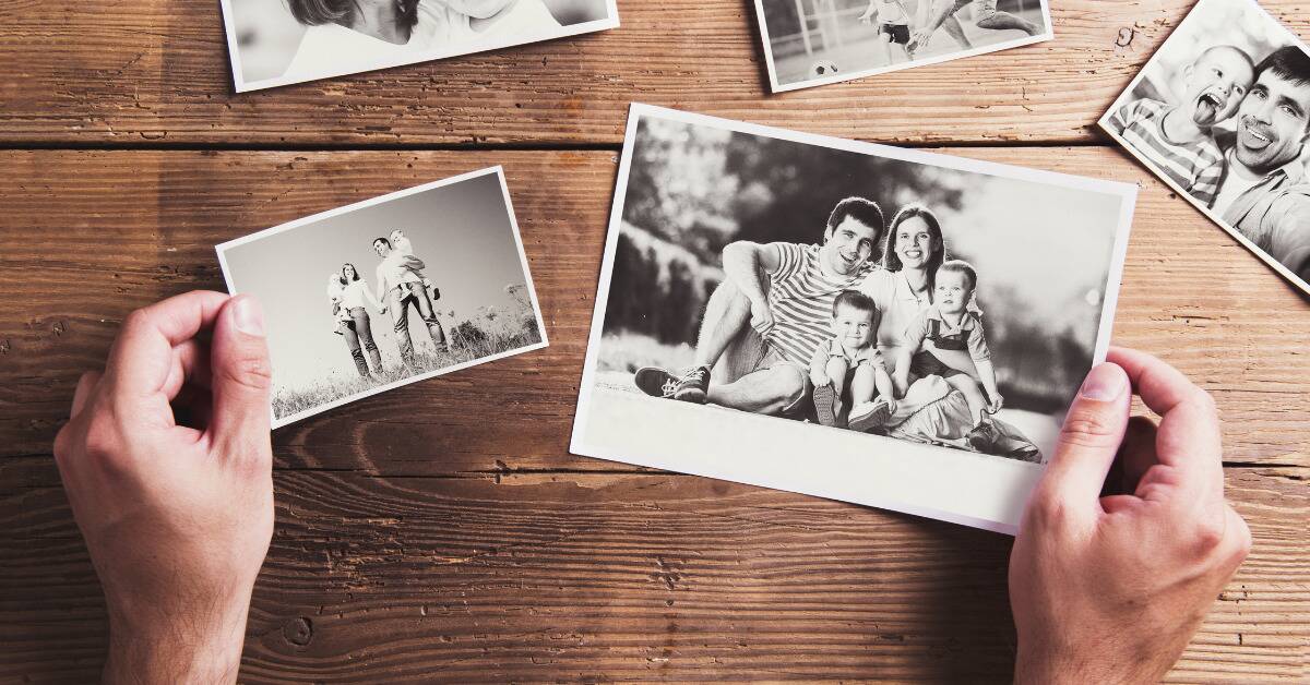 Two hands holding out printed greyscale family photos overtop a wooden table.