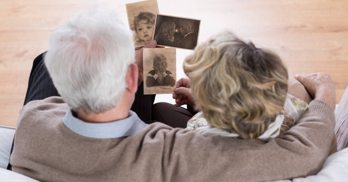 An older couple sitting next to each other, looking at old photos of themselves as children then of them as a young couple.