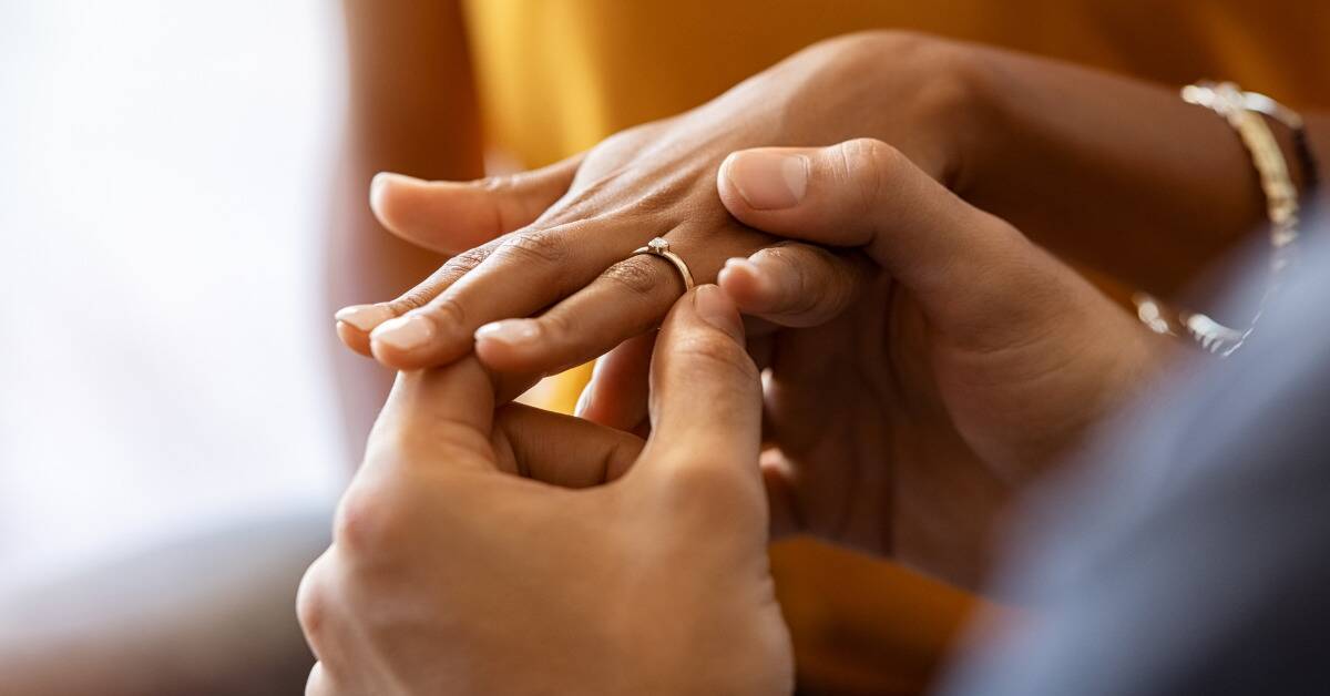 A close shot of a man sliding an engagement ring onto a woman's finger.