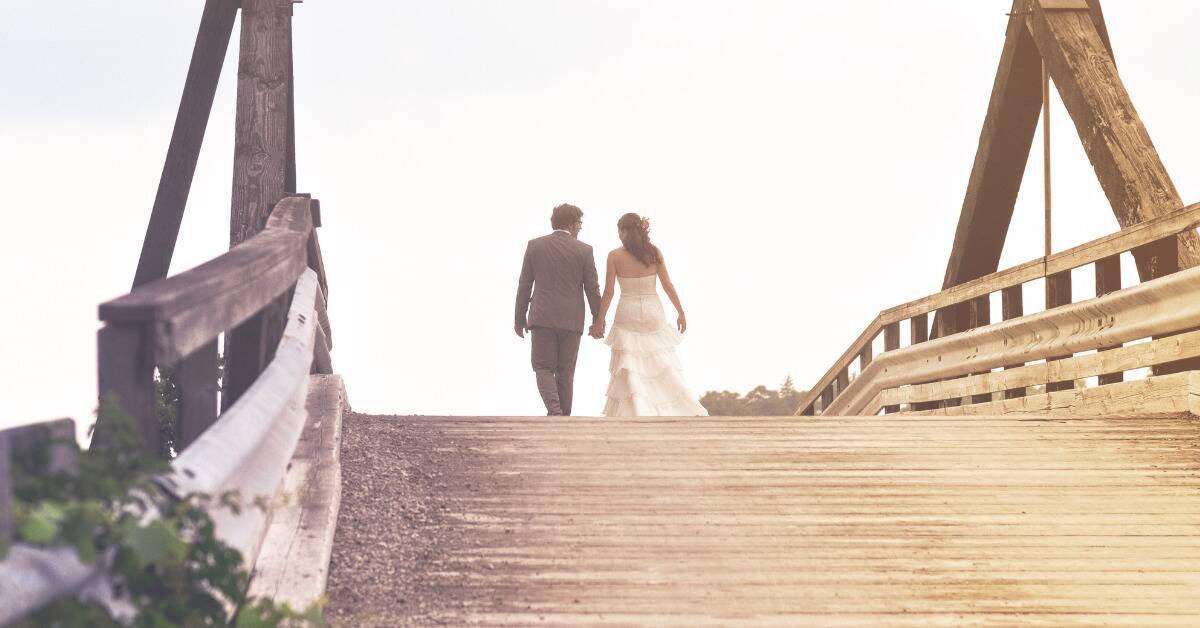 A bride and a groom holding hands, walking away from the camera over a bridge.