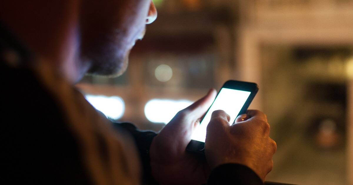 A close shot of a man looking at the glowing screen of his cell phone.