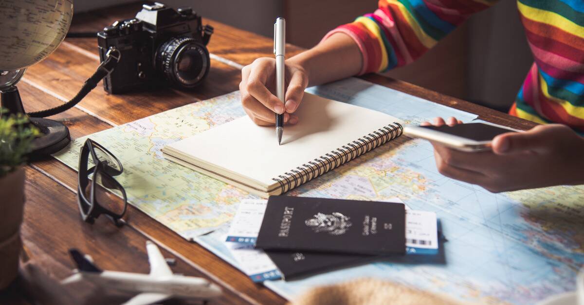 Someone writing in a journal atop a map, passports placed next to them.