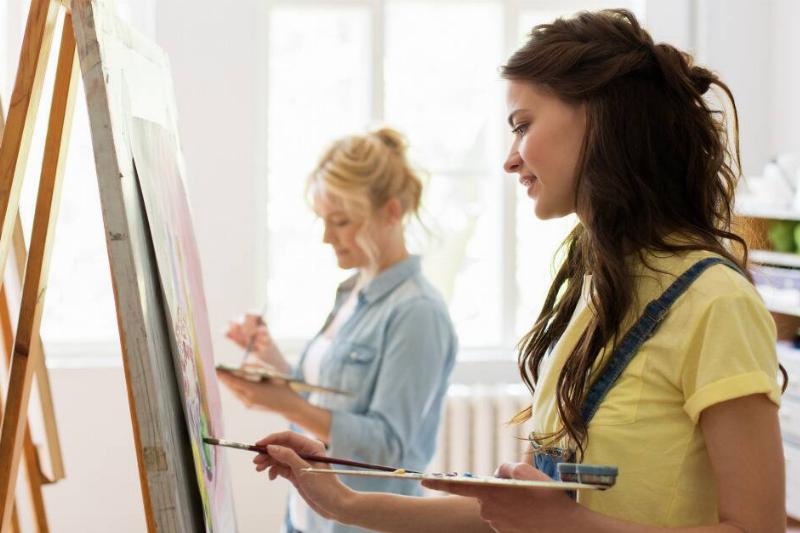 Two women standing at easels, both in a painting class.