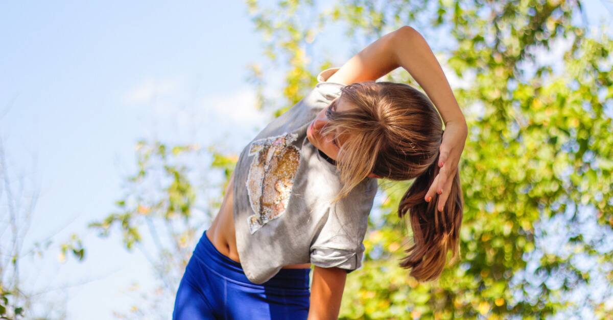 A woman stretching as she stands outside.