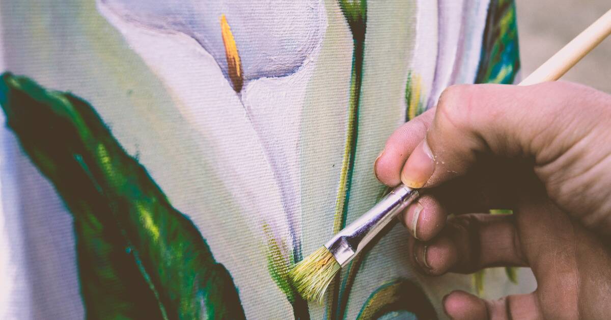 A close shot of someone painting a flower on a canvas.