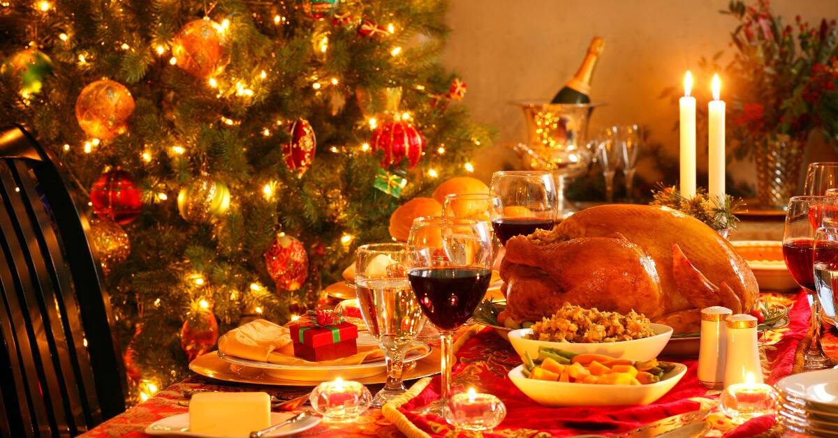 A table set with Christmas dinner, a large decorated tree in the background.