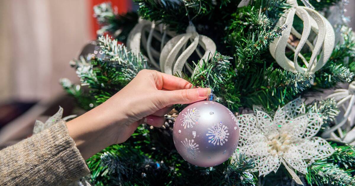 A close shot of a woman putting a silver ornament on a Christmas tree.