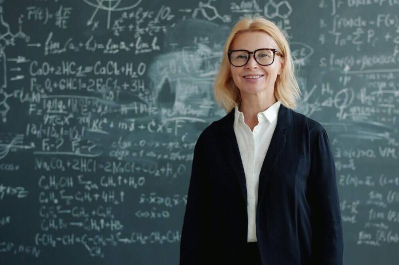 A woman standing in front of a chalkboard full of advanced functions and equations