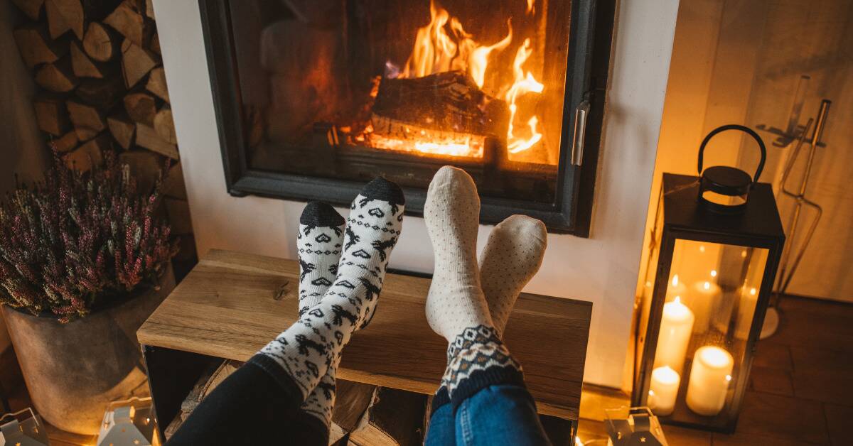 Two pairs of feet in cozy socks kicked back in front of a fireplace.
